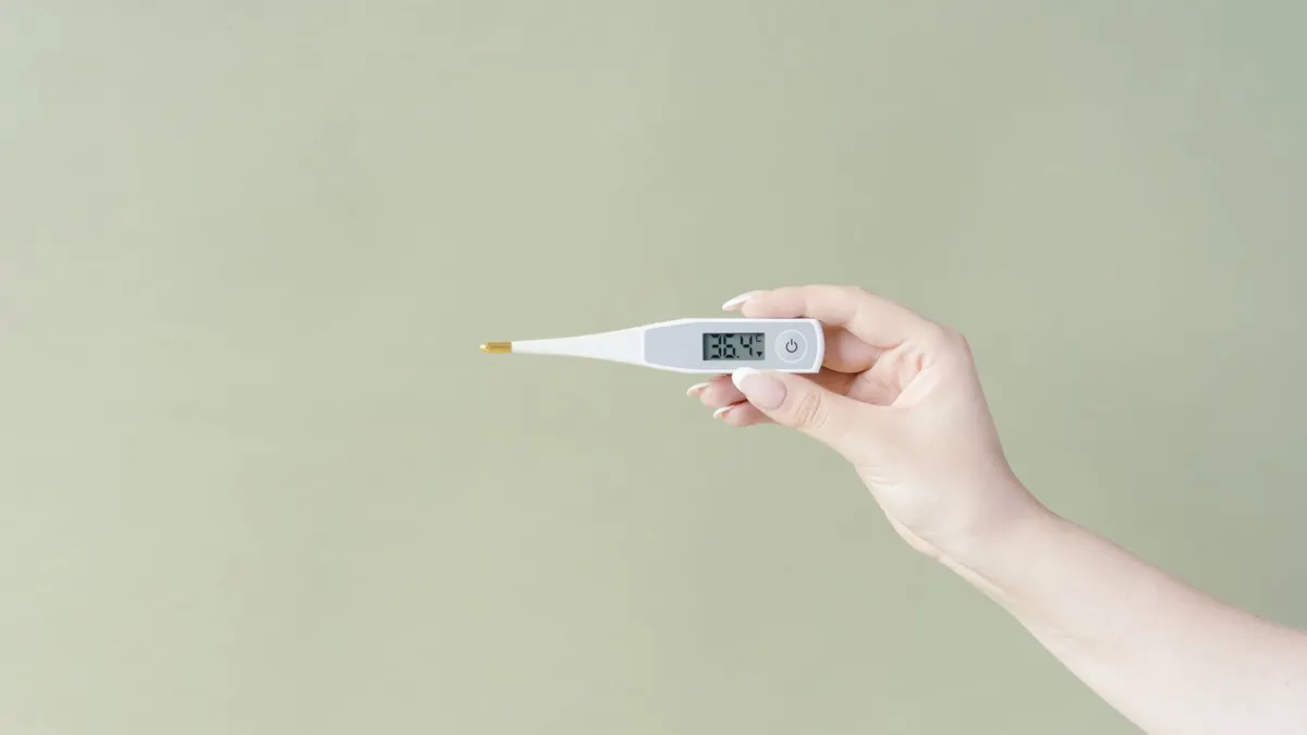 Hand holding a digital thermometer displaying 36.4°C on a light green background, minimalistic style.
