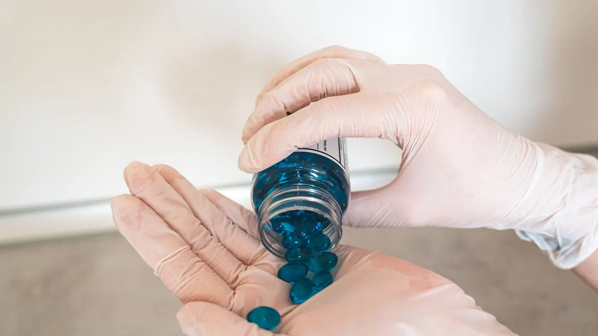 Close-up of hands in gloves pouring blue pills from a bottle, symbolizing medication and healthcare.