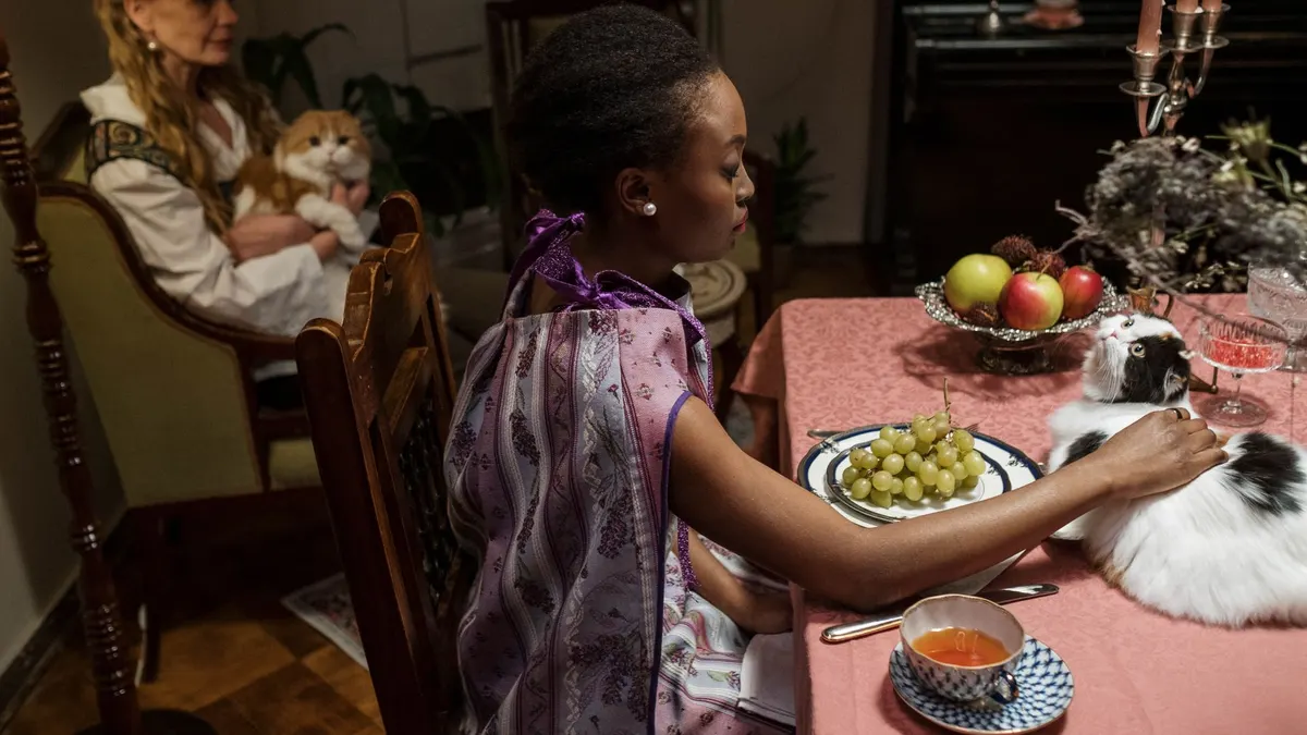 Charming indoor dinner scene with women, cats, and a table set with fruits and tea.