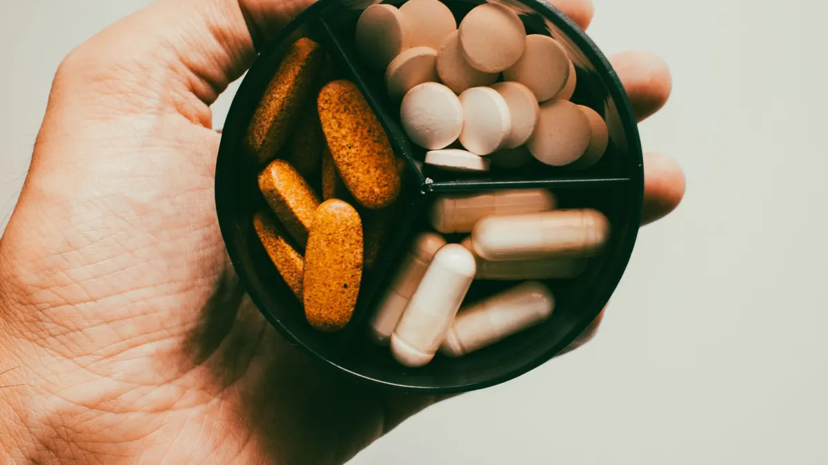 Close-up of a hand holding different types of supplements and vitamins.