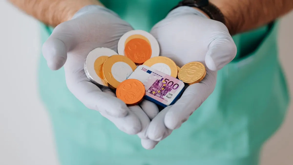 From above crop anonymous medical worker in rubber disposable gloves holding in hands chocolate coins