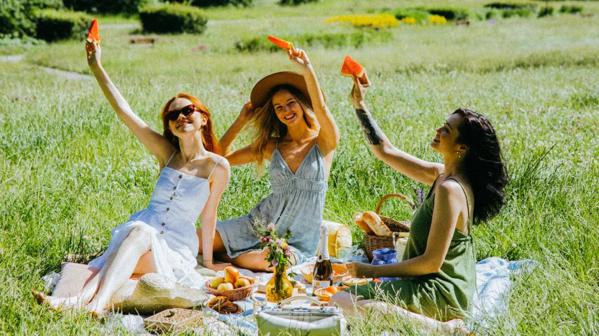 Three cheerful women having a summer picnic with watermelon slices in a sunny meadow.