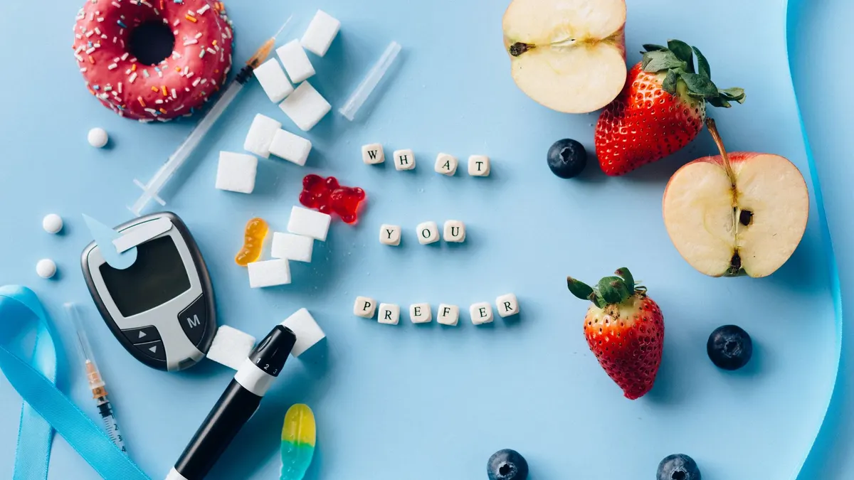 A creative diabetes awareness still life with insulin syringe, fruits, donut, and glucose meter on blue background.